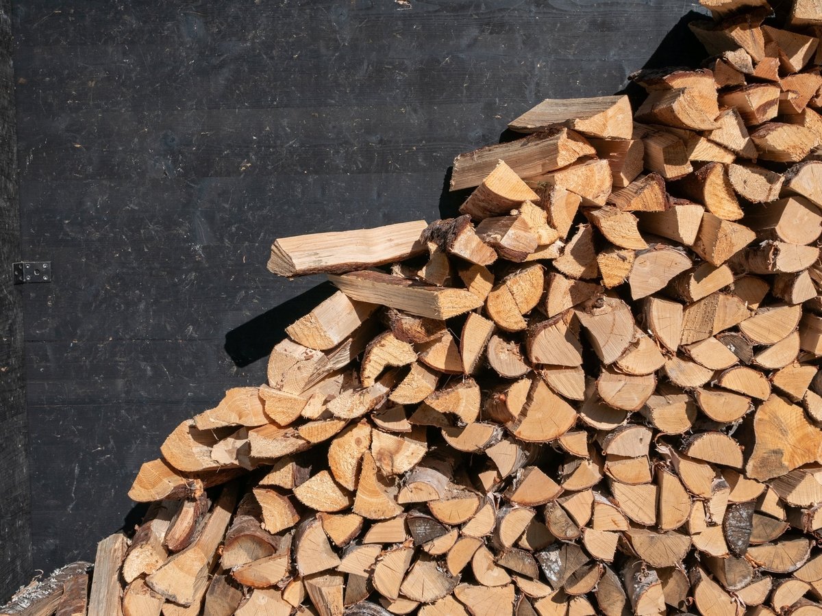 Neatly stacked chopped firewood against a house wall in warm sunlight